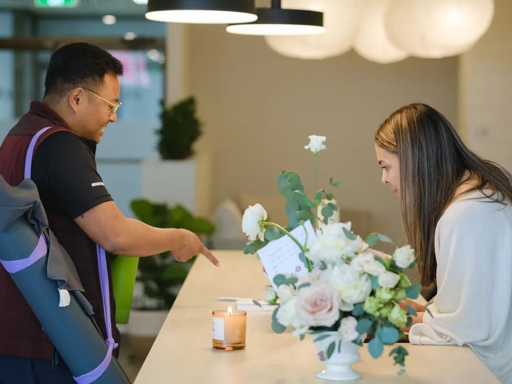 A member being greeted at the front desk beside fresh flowers.