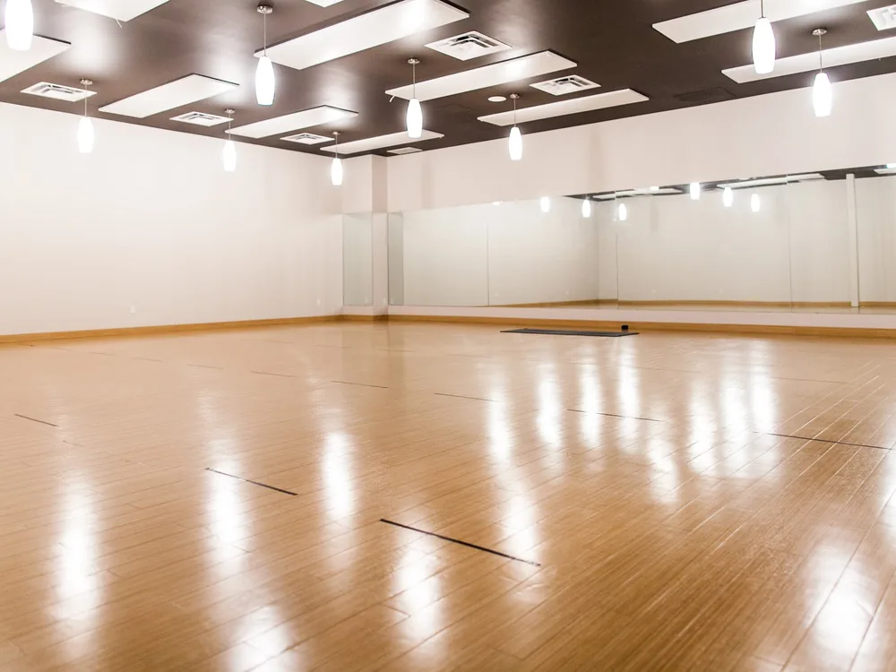 Late light across the wood floor of the empty South Edmonton practice room, mirrors along one wall.