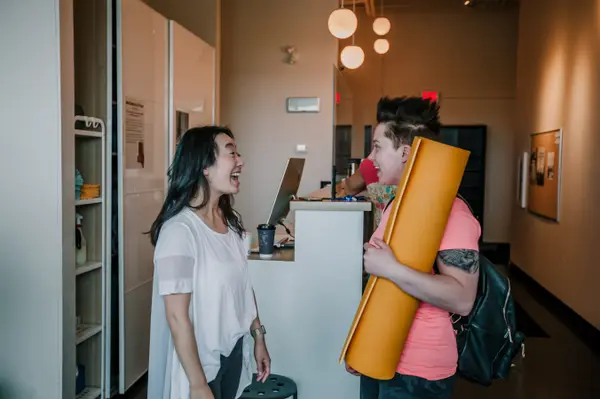 A member checking in at the front desk with a rolled mat under their arm.