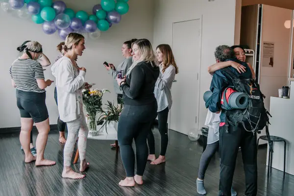 Members gathered under a balloon arch, hugging and talking.